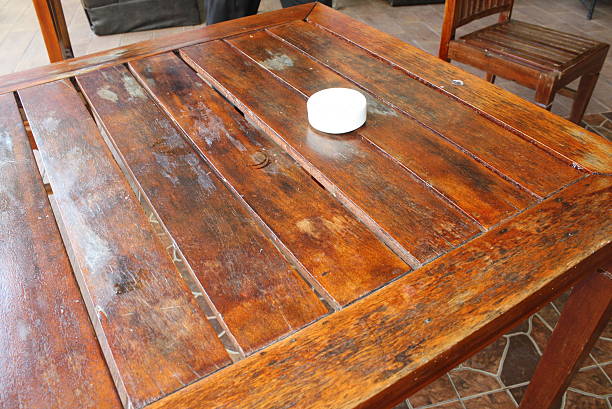 Rustic wooden table with slatted planks displays signs of wear, including scratches and water stains, under natural light