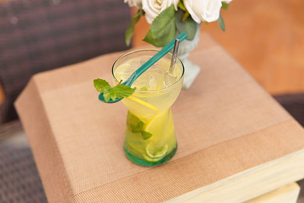 Refreshing lemonade with mint, lemon, and lime slices, served with ice and a reusable straw on a textured placemat White roses are in the blurred background