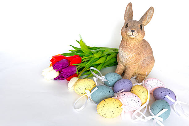 Easter bunny surrounded by multi-coloured decorated Easter eggs and fresh tulips on a white background with lots of copy space.
