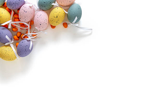 Various sized multi-coloured decorated Easter eggs with white ribbons arranged at the top corner of a white background leaving plenty of copy space.
