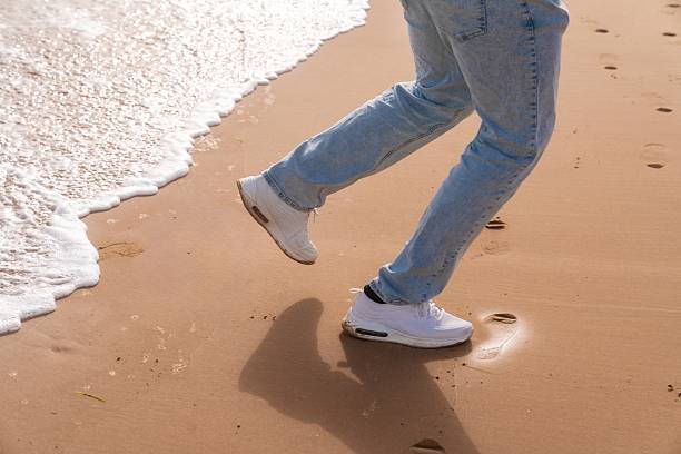 Steps leaving impressions on damp sandy coastlines. Foot marks recorded along moist sandy edge of shoreline. Distinct footprints indicating athletic movement along wet and sandy coast boundary