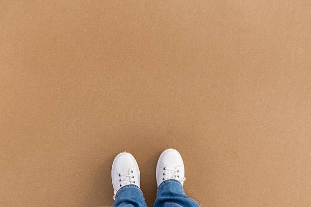 Traveler pauses footwear on sunny beach. Gentle morning light highlights casual footwear on dry sands scene. Overhead view captures relaxed traveler with sneakers resting on sunlit sandy surface