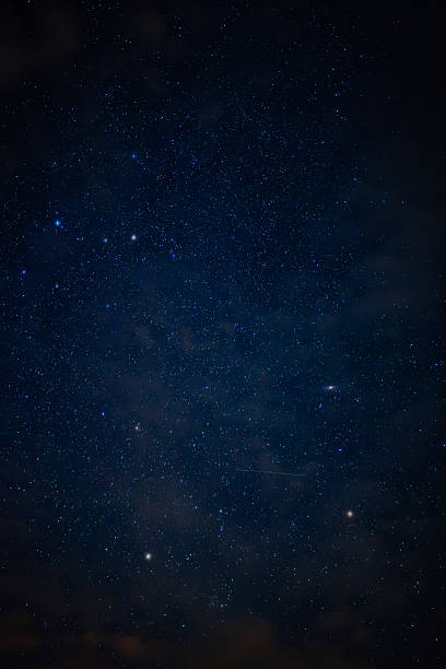 A serene night sky filled with countless stars and drifting clouds. A faint streak, possibly a shooting star or satellite, adds dynamic detail.