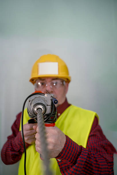Construction worker wearing hard hat and safety vest operating a heavy duty drill