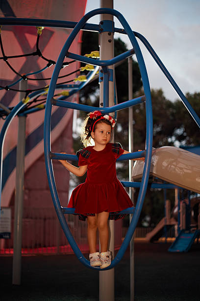 Little girl in red dress standing on a blue climbing structure at a park