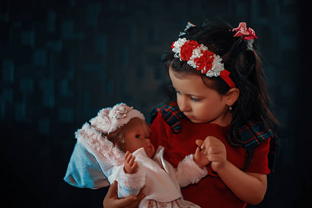 Young child holding and looking at her doll, representing childhood care and nurture