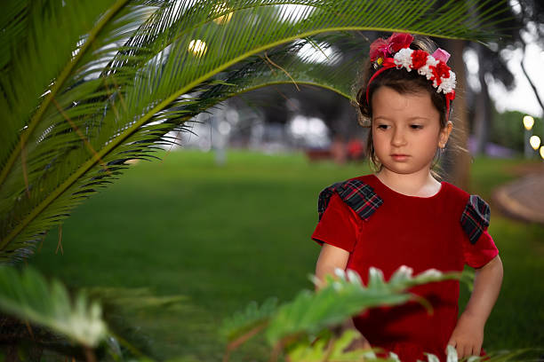 Little girl wearing red dress with colorful headband standing outdoors