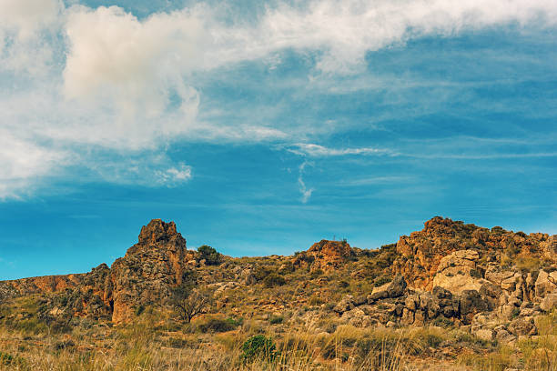Arid rocky rough landscape with some vegetation and trees under a blue sky with some clouds. Huebro, Almeria, Andalusia, Spain.