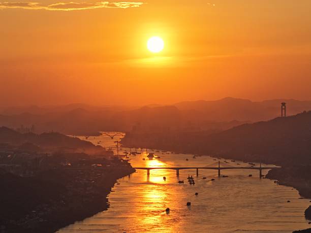 Sunset over a river with bridge and distant hills, reflecting golden light on water