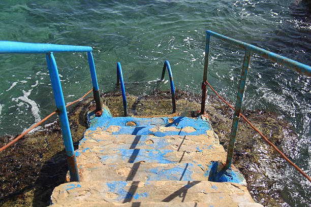 Weathered stone stairs, with rusty blue rails, descending directly into the Mediterranean Sea in Anfeh, Lebanon.