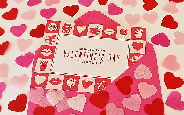 High-angle view of a Valentine's Day greeting card on a pink envelope surrounded by heart-shaped paper decorations. Valentine's Day greeting card.