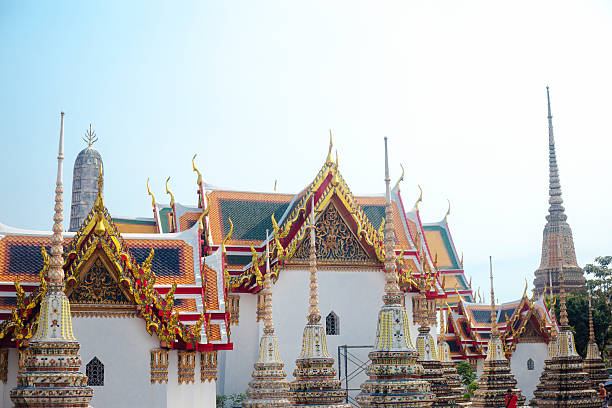Buildings and temples of Wat  Pho in Bangkok Phra Nakhon at afternoon light. View over surrounding  wall from street Thai Wang  Road.In bottom area people and trousits are walking among buildings of monastery ground