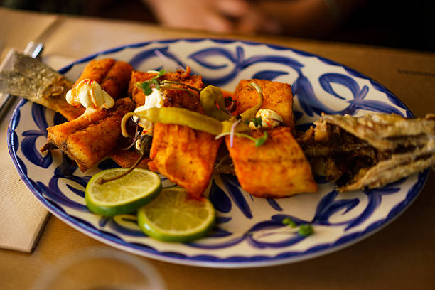 Fried white fish fillets and whole fish garnished with lime, sauce, and peppers