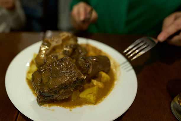 Person enjoying a hearty oxtail stew with tender meat, rich gravy, and potatoes