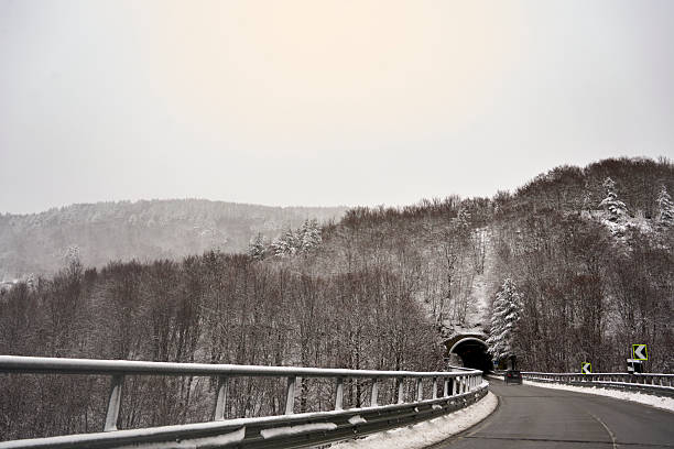 Snow-covered guardrail on a winding road leading to a tunnel entrance within a winter mountain landscape