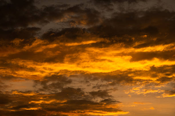 The sky is filled with dark clouds mixed with orange tones as the sun sets on the horizon. This evening scene highlights the changing colors of the sky at dusk.
