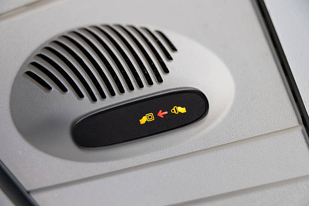 Closeup of an airplane cabin overhead panel with an illuminated fasten seatbelt indicator and speaker grille, showing passenger safety signage and controls inside a modern commercial aircraft