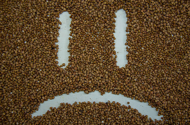 Buckwheat groats arranged in a sad face emoticon on a white surface, symbolizing sadness using natural food elements.