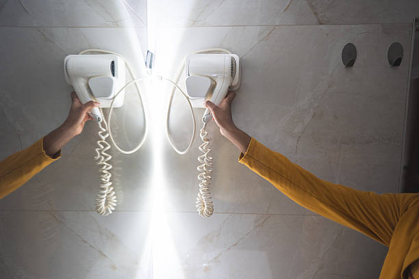 Latin American female standing in front of a mirror while drying her hair using hair dryer after washing and treating her hair at the decorated bathroom before going to work.