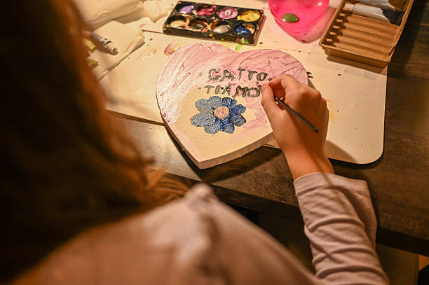 Child's hand painting a heart-shaped craft with GATTO TI AMO and a flower