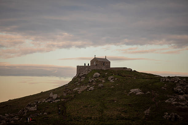 St. Ives, England – December 27, 2025: St. Nicholas Chapel sits atop a rocky hill overlooking the coast, with visitors nearby under soft afternoon light. Editorial use only; no release required.