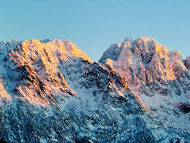 Austvagoya Lofoten Mountain Ridge Norway in colorful Sunset Light in Winter. Illuminated Mountain Peaks of the Lofoten Islands against blue twilight sky. Moody Wintercolors in Northern Norway. Austvagoya, Lofoten, Northern Norway, Northern Europe, Nordic Countries.