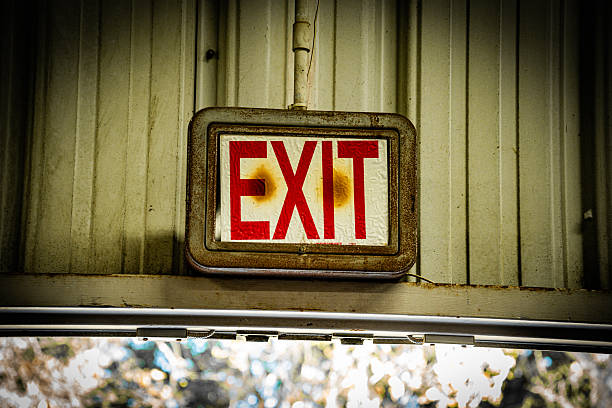 An old, weathered exit sign with visible rust and stains, mounted on a textured industrial wall, suggesting a sense of decay and history