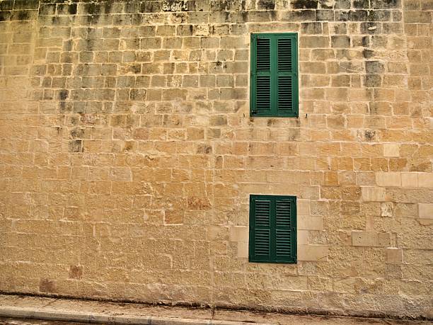 Traditional Maltese limestone wall with two green louvered window shutters