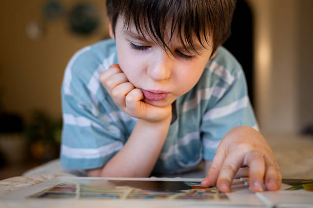Close-up of a young boy reading a picture book at home, resting his head on his hand. Concept of childhood education, concentration, early learning, quiet family lifestyle and cognitive development.