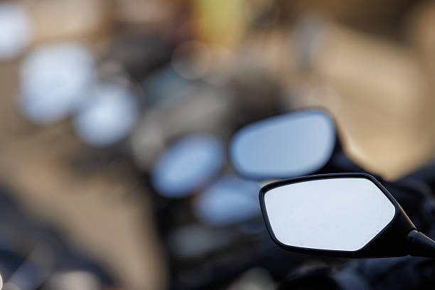 A close-up of parked motorcycle side mirrors. The focus is on the foreground mirror, while other mirrors are blurred in the background, creating a rhythmic sense of depth.