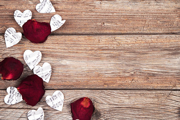 Paper hearts with notes and red rose petals on wooden table