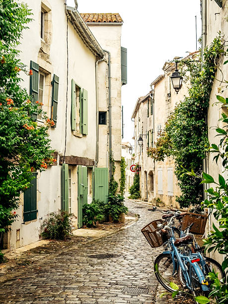 Bicycles resting along a narrow cobblestone street lined with white houses, green shutters, and climbing plants on the Île de Ré, France, evoking slow travel, everyday European life, and summer calm.