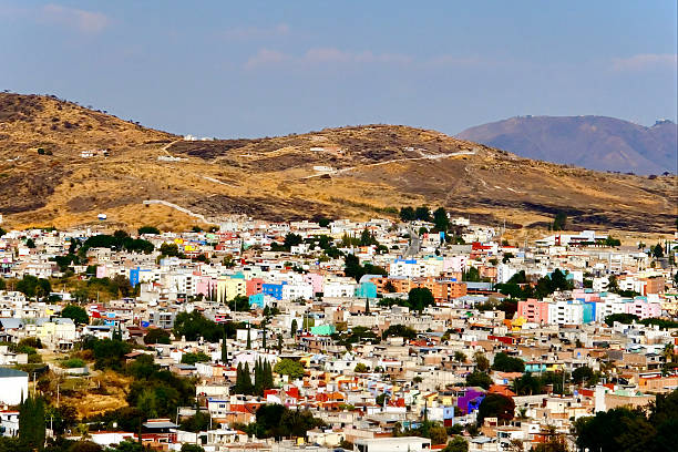 Small colorful houses dot the hills beneath dry mountains, capturing the expanding outskirts of a provincial highland city.