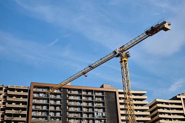 A large yellow tower crane stands over a multi-story residential building under a clear blue sky