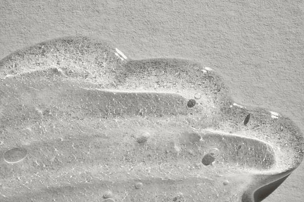Transparent gel, serum, or liquid moisturizer spreading on a textured grey background