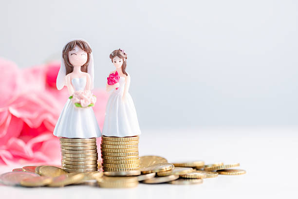 istock Inclusive wedding savings concept with two bride figurines on stacked coins, pastel pink flowers and copy space, celebrating diversity, equality, shared financial planning for couples. wedding savings 2260478655