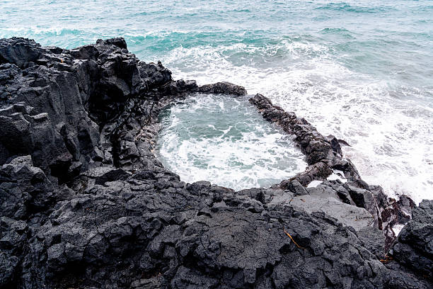 Brimketill lava pool on the stretch of coast with black volcanic rocks and rough seas in the Reykjanes Peninsula in Iceland during a spring day.