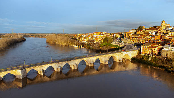 The waters of the Duero River overflow and flow under the historic stone bridge that heroically resists the force of the waters, in Valladolid, Spain, at sunrise.
