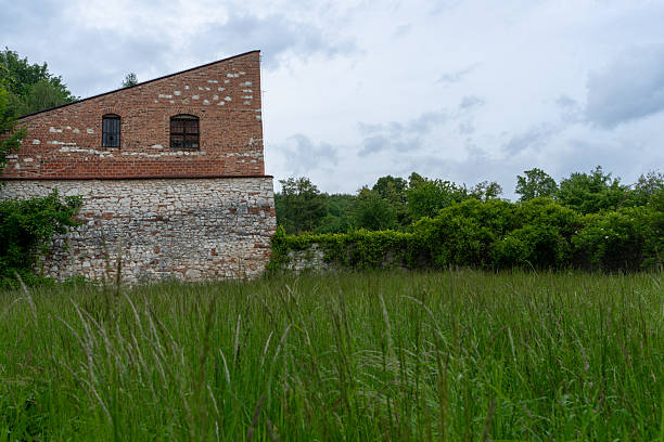 Krakow, Poland – May 23, 2025: A section of brick and stone wall from the Tyniec Abbey complex borders a grassy meadow. The contrast between structured masonry and natural vegetation defines the historic surroundings.