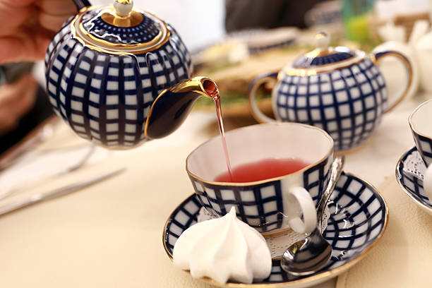 Woman pouring hot fruit tea from elegant blue and white teapot into a teacup for afternoon tea ceremony at a cozy café