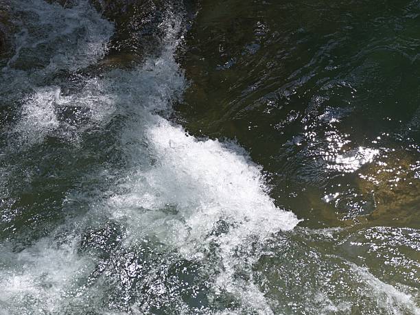 Aerial view of rushing water creating white foam as it flows over rocks in a river