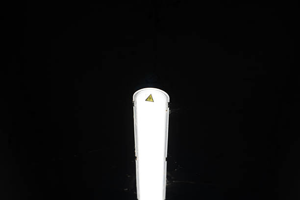 A bright light fixture hangs from the ceiling, casting light against a dark background. The simple design features a warning symbol, creating a striking contrast.