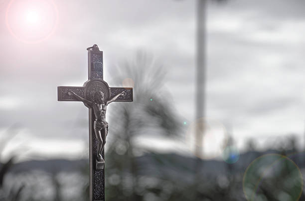 Dark silhouetted holy cross photographed in monochrome tones with dramatic sky creating a moody atmosphere of faith sacrifice and solemn remembrance