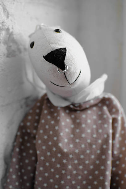 A gray soft toy cat in an embroidered coat is sitting on a sofa leaning against a gray shiny pillow. The topic of toys in the Ukrainian style.