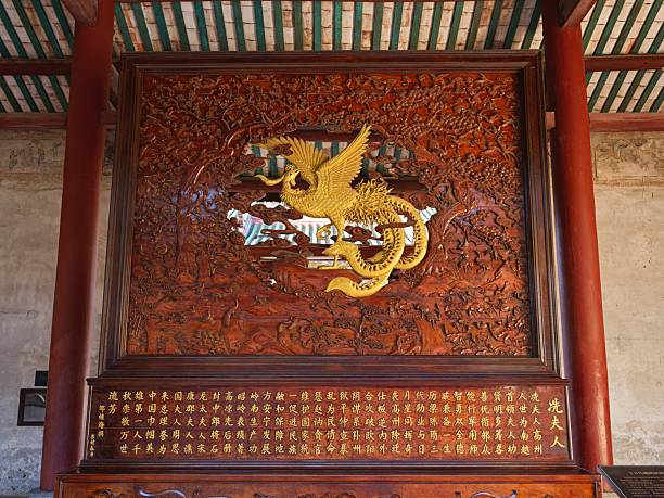 Intricately carved wooden panel featuring a golden phoenix amidst floral patterns, displayed within a traditional architectural setting.
