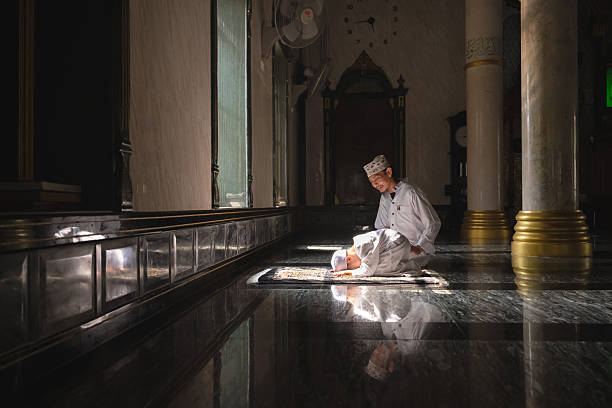 A Muslim father in traditional white clothing gently teaches his young son the steps of prayer (salah) inside a mosque, captured in warm natural light with a clear reflection on the polished floor, expressing family bond, faith, and religious education.