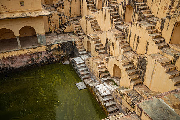 Old Indian stepwell with symmetrical stone stairs and murky green water.