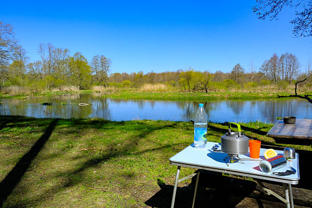 Riverside campsite with kettle, orange cup, and spring trees by stream