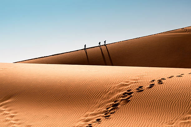 silhouettes of three people climbing up big daddy in Sossusvlei desert area