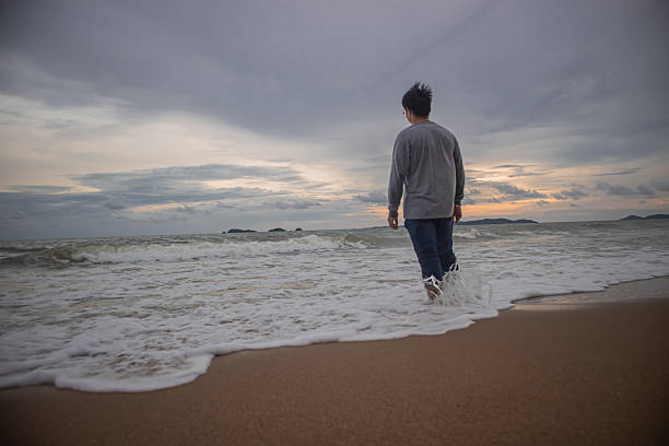 Man standing in ocean waves at sunset, dramatic sky, facing challenges, courage and resilience concept, solitude, reflection, life journey.